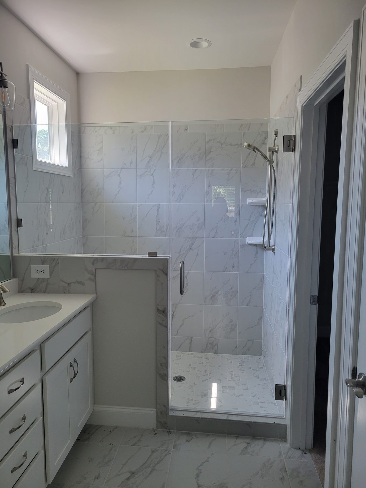 A walk-in shower with marble-look tile and a glass door beside a white vanity