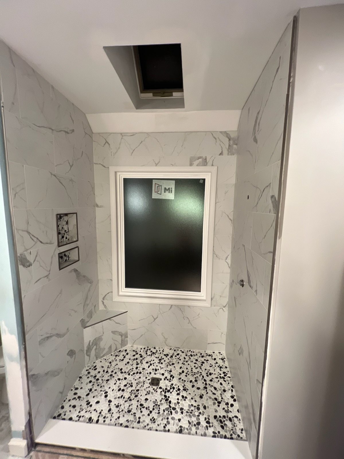A tiled shower with a window, built-in niche and pebble floor