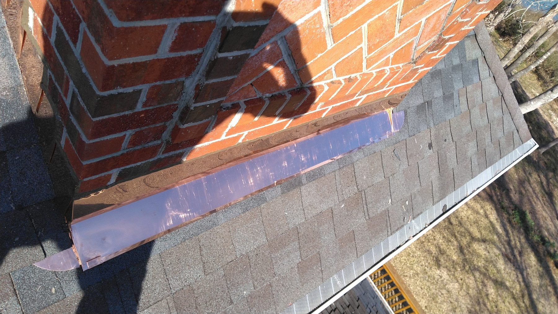 New copper flashing stepped into a brick chimney on a shingle roof