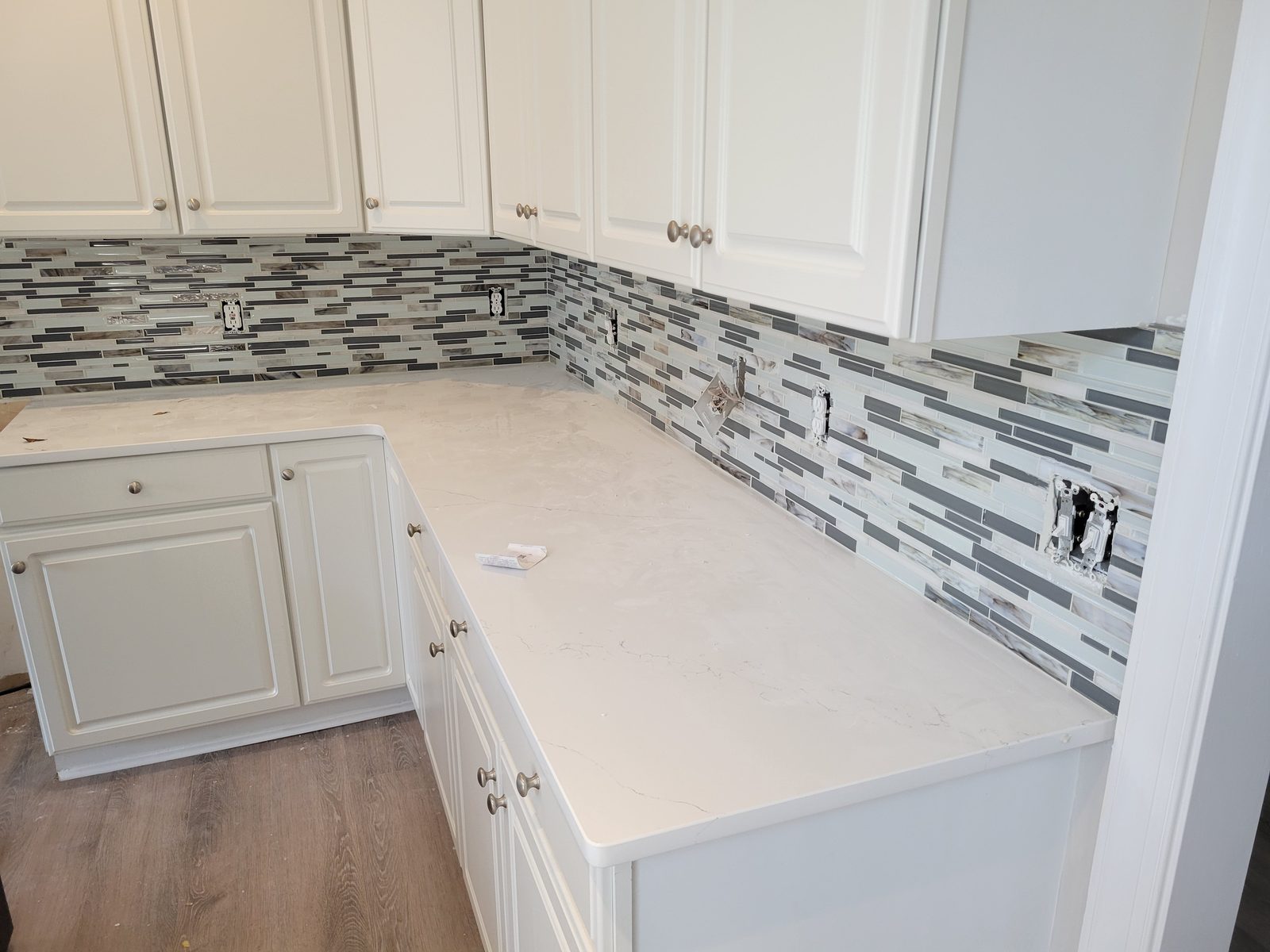 White cabinets with a glass mosaic tile backsplash and light countertops