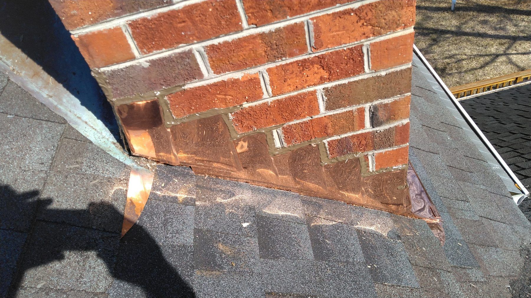 Copper flashing where a brick chimney meets a shingle roof
