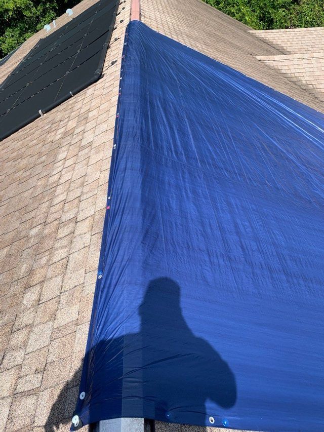 Blue emergency tarp secured over a damaged roof section