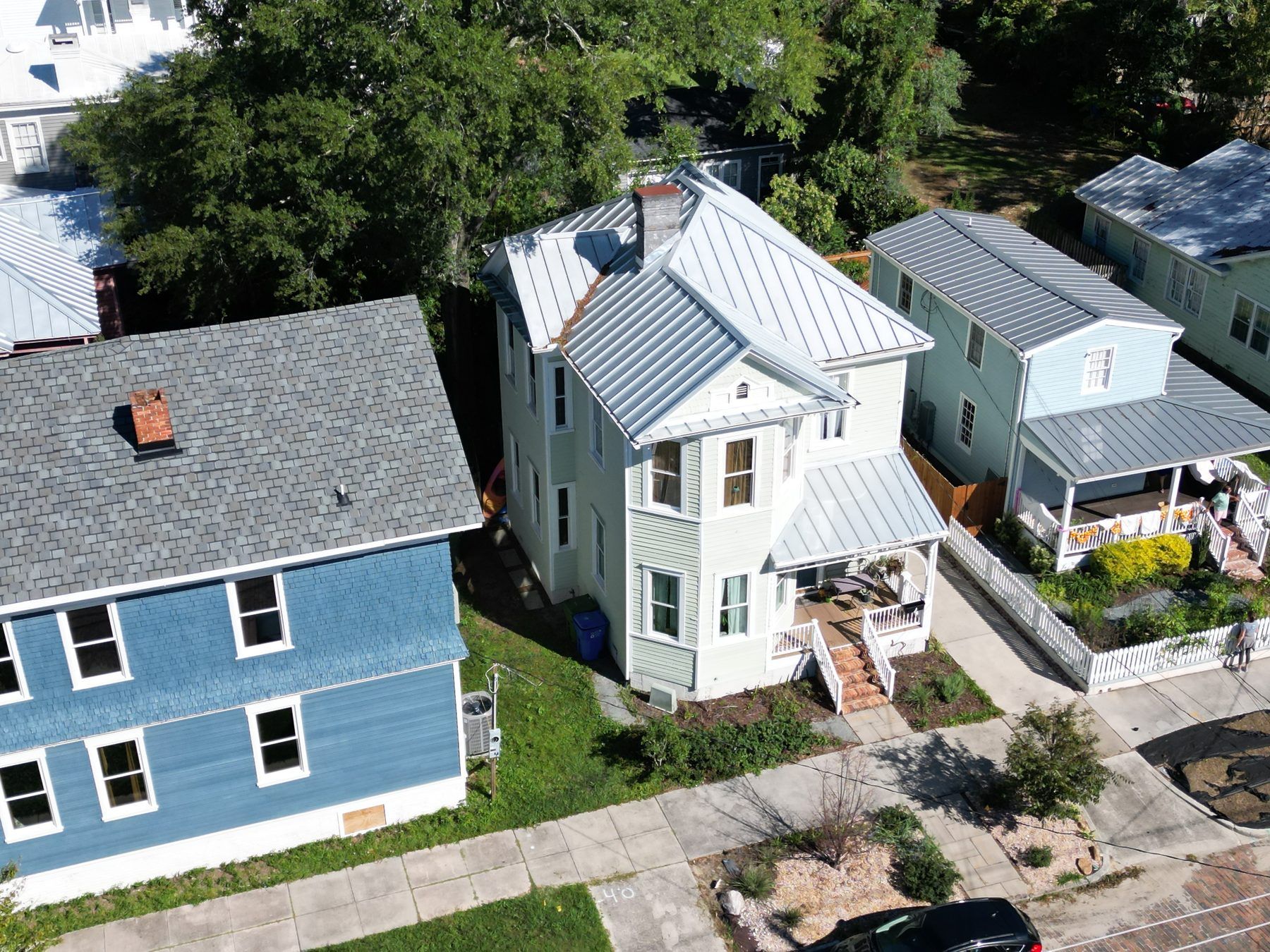 Older-style blue cottage with a silver metal roof among neighboring homes, from the air