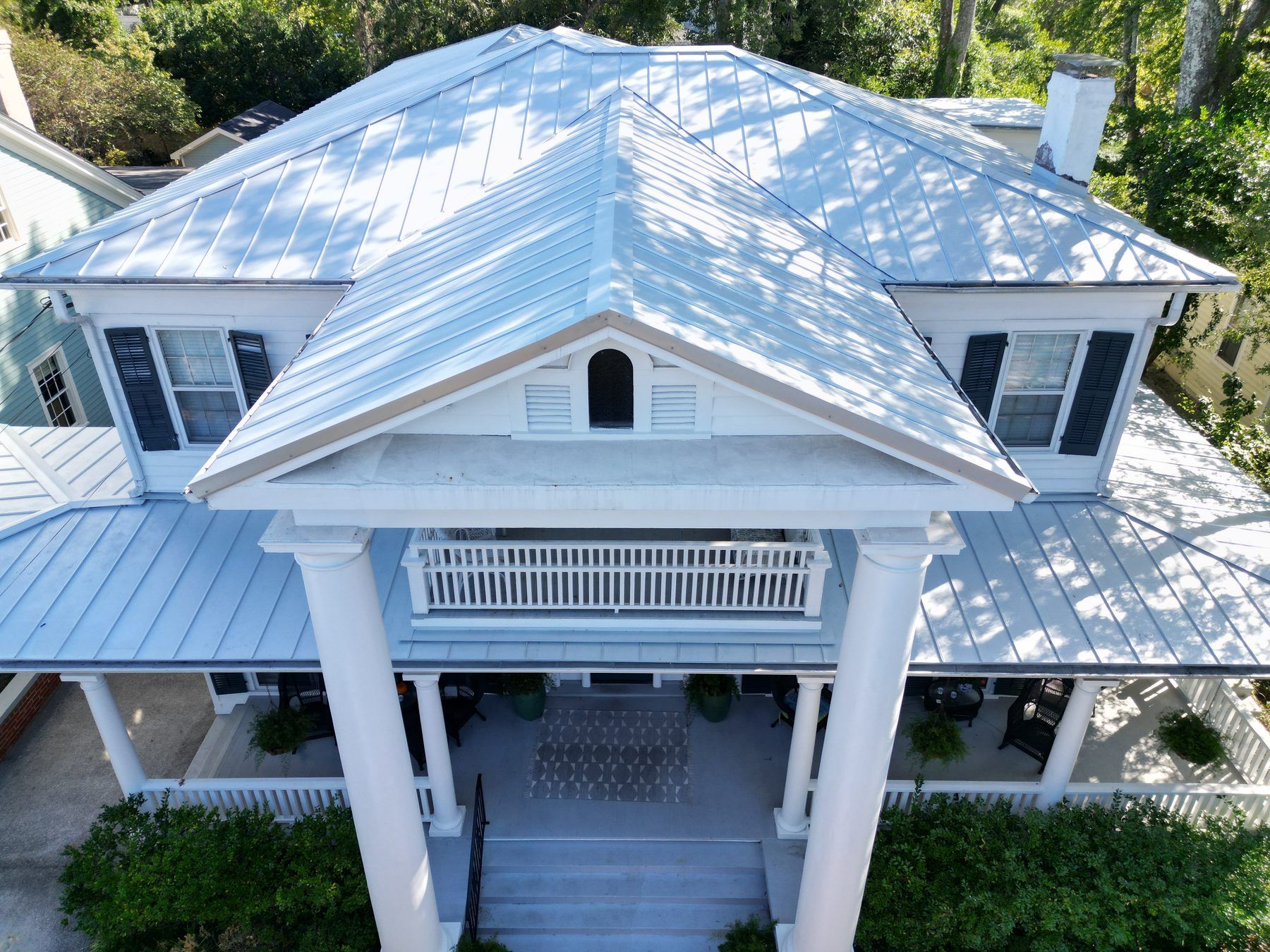 Large white coastal home with a columned portico and a white standing-seam metal roof, from the air