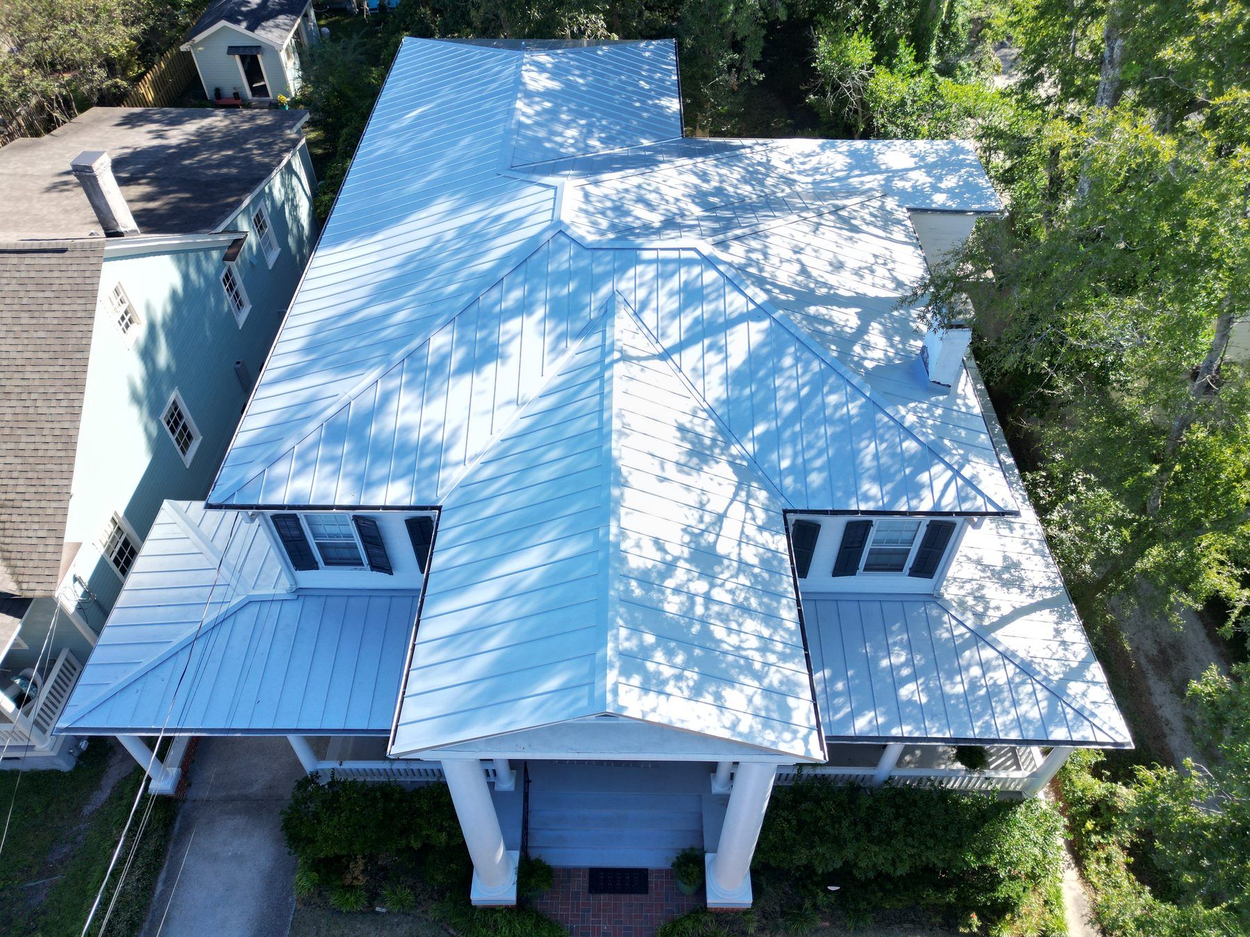 White standing-seam metal roof on a coastal home, from high above