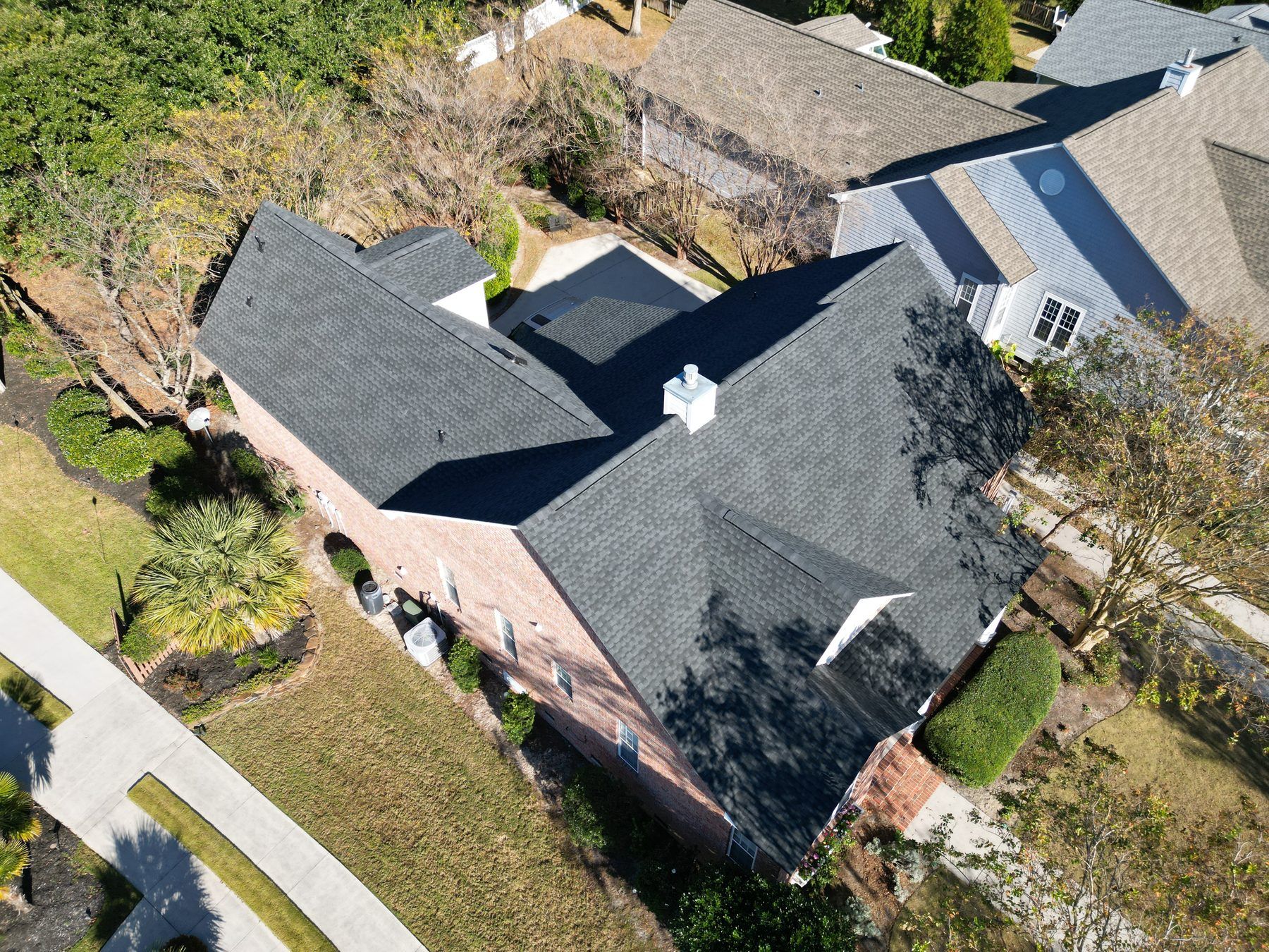 Brick home with a new charcoal architectural shingle roof, seen from the air among trees