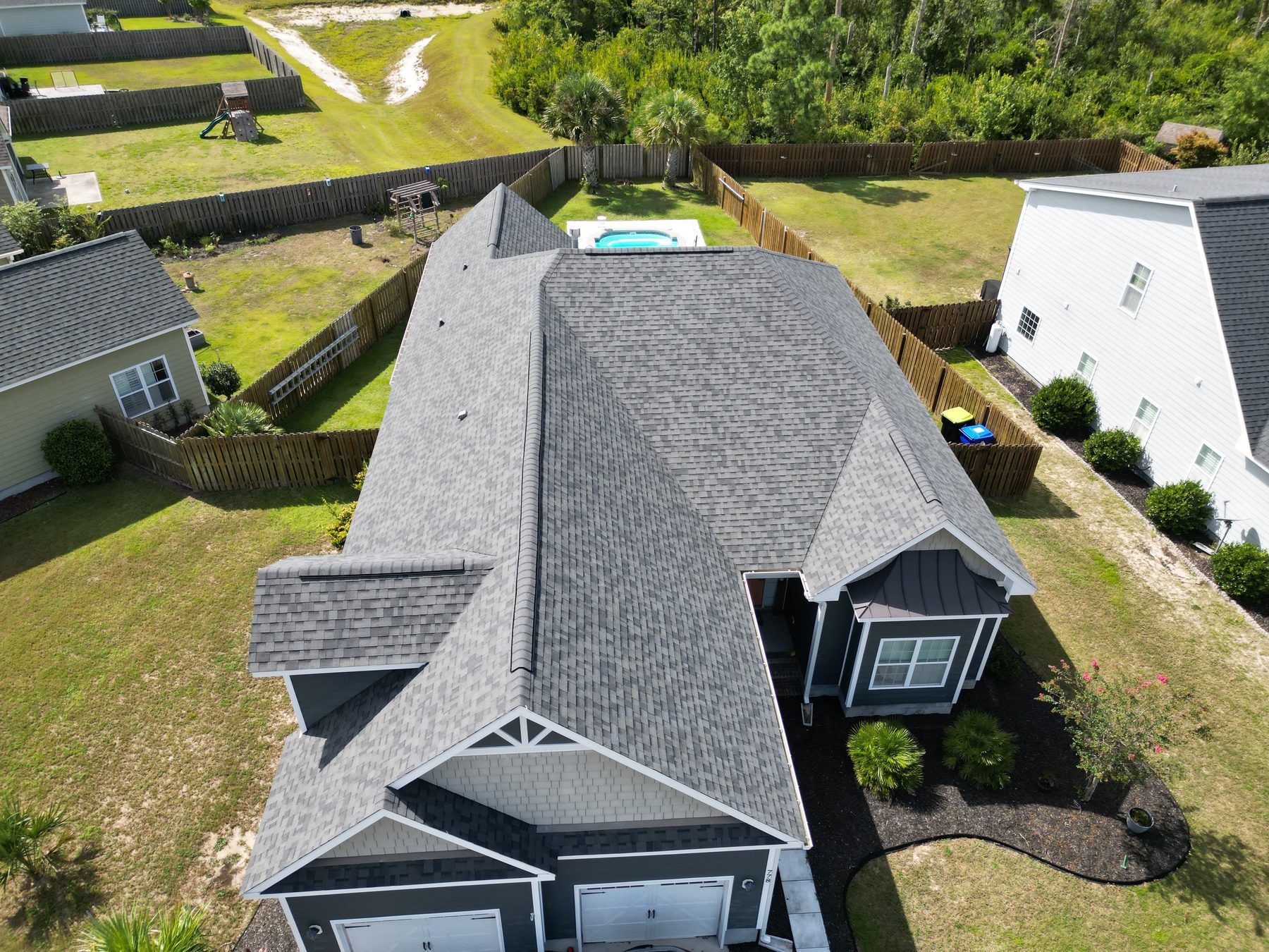 Blue-grey home with a gray shingle roof and a pool, from the air