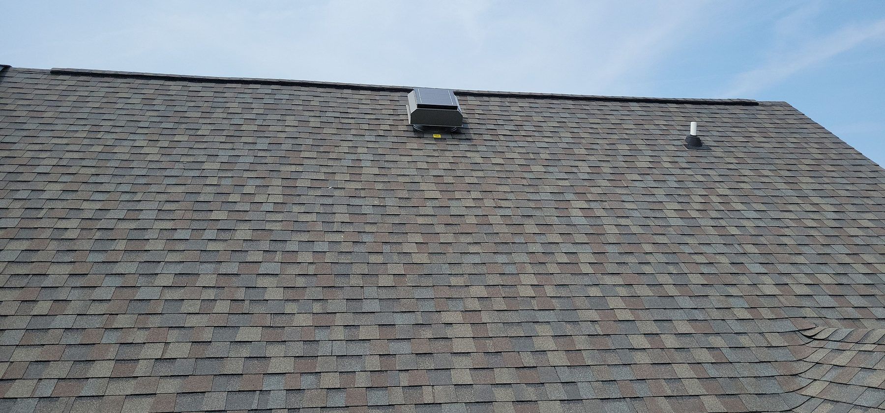 Solar attic fan installed near the ridge of a shingle roof