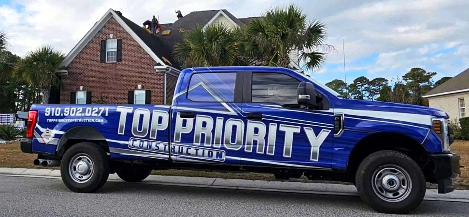 Blue TPC truck at a brick home while crew work on the roof